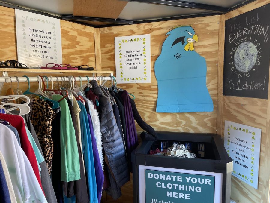 Coastal has clothes ready to sell hanging up and a donate bin in their converted storage unit. The club promotes sustainability efforts with their signs. 