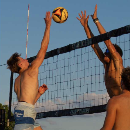 CCU club beach volleyball player attacks the ball while another blocks.